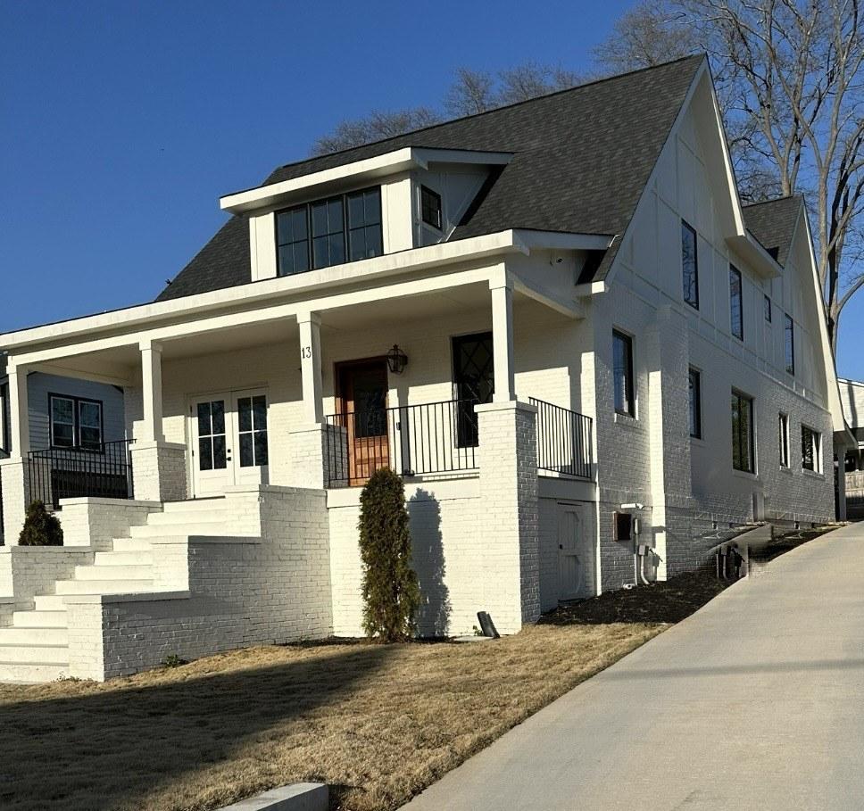 White painted-brick custom home by Blackstock: deep front porch with columns, black-framed windows, gabled dormer, and a wood front door, under a clear blue sky.
