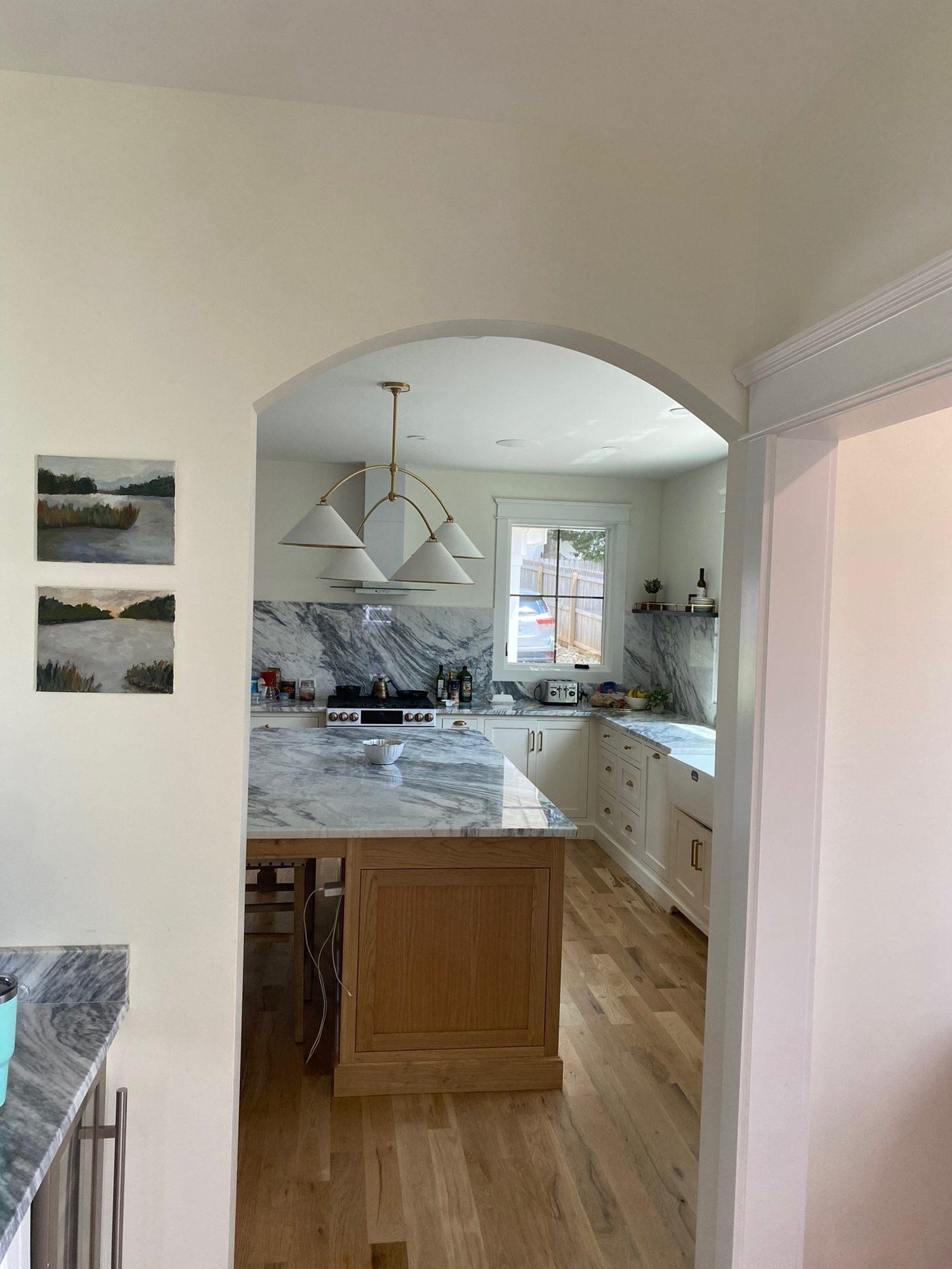 Arched cased opening framing a view into the kitchen, with marble surfaces, a brass pendant, and white oak floors.